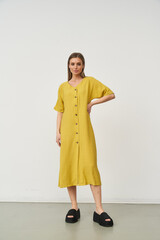Stylish female model poses in a fashionable yellow dress inside a studio setting