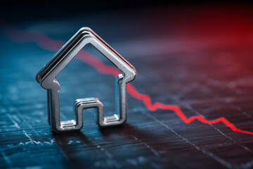 Metal house outline with falling red line on graph background depicting economic downturn concept image