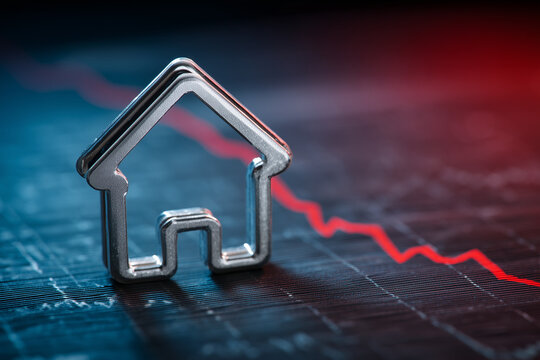 Metal house outline with falling red line on graph background depicting economic downturn concept image