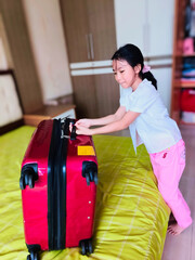Suitcase Struggle. A Little Girl's Determination Shines Through as She Tries to Lift a Big Suitcase, Showing She's Ready for a Fantastic Family Holiday Adventure.