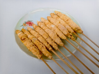 Egg rolls with bamboo skewers on a white plate on a white background. Indonesian street food.