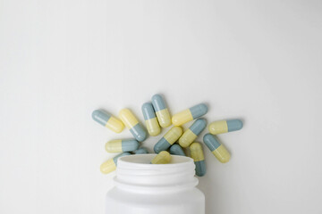 Top view white bottle container with medication capsules on light grey background with copy space.