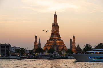 Naklejka premium Wat Arun Ratchawararam Ratchawaramahawihan (Temple of Dawn) with a tourist on a cruise boat capturing a photo in a magical moment along the Chao Phraya river at twilight in Bangkok, Thailand.