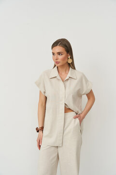 Model in beige short-sleeve shirt and wide-leg pants against plain backdrop. Fashion-forward look with minimalistic style, accessorized with large earrings and a bracelet