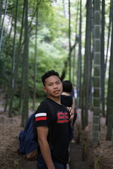 Naklejka premium Young man glances back while exploring the serene beauty of a bamboo forest path on a nature walk