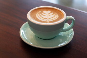 Cup of coffee with latte art on wooden table with soft sunlight.
