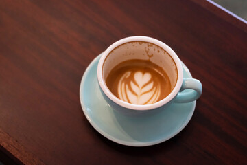 Cup of coffee with latte art on wooden table with soft sunlight. Perfect latte art on the bottom of cup.