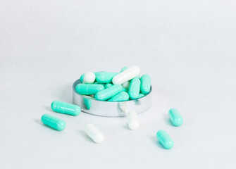 Selective focus of green-white capsule pills in a stainless container, scattered on a clean surface with copy space, showing modern healthcare, medication, and pharmaceutical supplement concept.