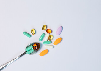 Top-view colorful pills and multivitamins with spoon on white background. Lay flat composition with copy space shows healthcare, daily supplement, and pharmaceutical lifestyle in clean, minimal style.