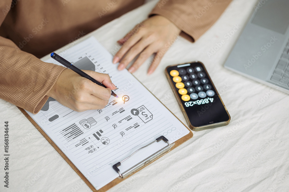 Poster a top-down view of a person analyzing financial charts on a clipboard, using a smartphone as a calcu