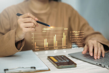 A person uses a laptop and a digital pen to analyze a holographic bar chart related to taxes.