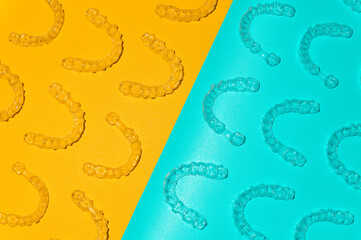 Transparent dental aligners on light blue and yellow background, close-up. Top view of pattern laid out from plastic braces for alignment. Background for advertising dental services