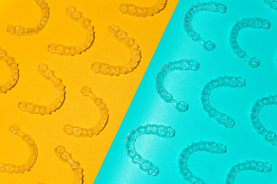 Transparent dental aligners on light blue and yellow background, close-up. Top view of pattern laid out from plastic braces for alignment. Background for advertising dental services
