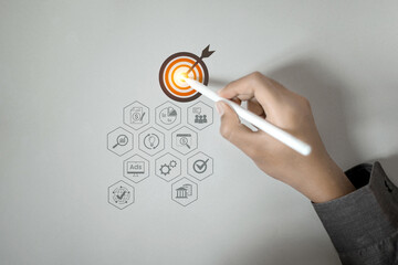 A hand uses a stylus to point at a target, with various business and marketing strategy icons...