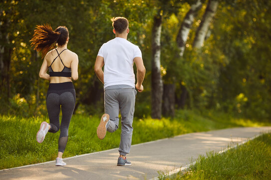 Sport workout and outdoor run of active couple, two fit people jogging in summer green park in morning. Back view of sporty woman and man running together along path. Sport training, wellbeing concept