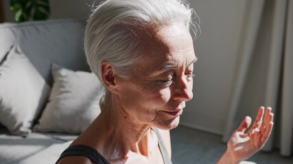 Senior woman meditating peacefully, sitting cross legged on sofa, practicing mindfulness with closed eyes, radiating calm and serenity indoors