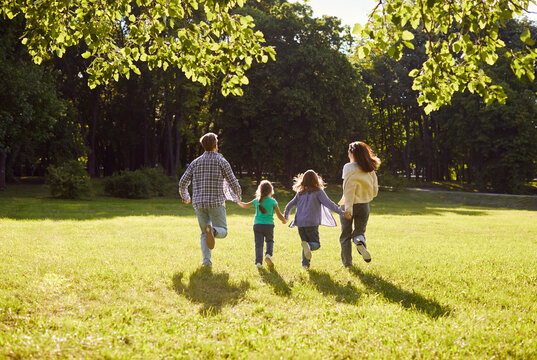 Back view of family with daughter and son walking outdoors enjoying beautiful nature. Mother, father with children running outdoors spending time together at sunset. Family leisure concept.