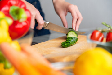 woman manually cuts a fresh cucumber, preparing it for cooking in a salad. chopping vegetables....