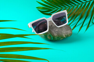 Trendy sunglasses on rock with palm leaves.