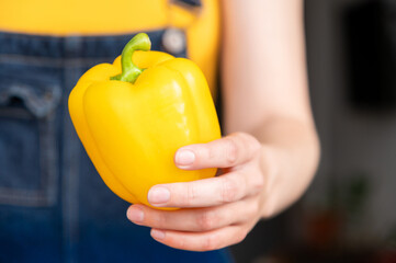 Close-up of yellow bell pepper in unrecognizable female hand. Girl hands pepper, sense of movement