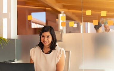 Portrait of a young working woman, of Asian features, smiles in the camera while working in the office