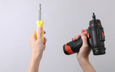 Female hands holding cordless screwdriver and screwdriver on gray background