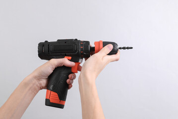 Female hand holding cordless screwdriver on grey background
