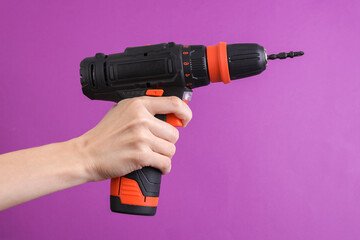 Female hand holding cordless screwdriver on purple background