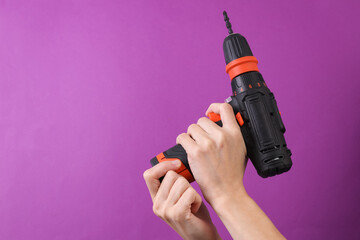 Female hands holding cordless screwdriver on purple background