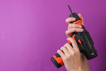 Female hands holding cordless screwdriver on purple background