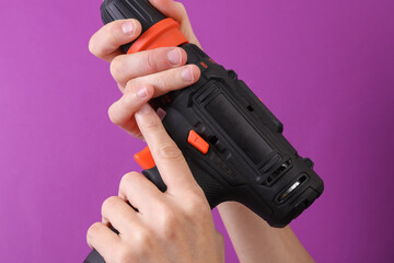 Female hands holding cordless screwdriver on purple background