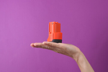 Female hand holding battery for screwdriver on purple background