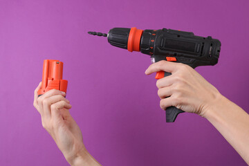 Female hands holding cordless screwdriver and battery on purple background