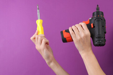 Female hands holding cordless screwdriver and screwdriver on purple background