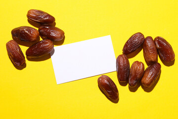 Dry tasty dates with white business card on yellow background
