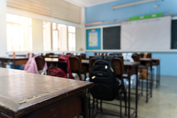 Vintage wooden desks and student backpacks in empty classroom with sunlight through windows education concept