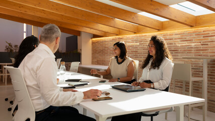 Several sitting people, women and men, discuss aspects of their work and the projects to be developed, during a meeting in the office