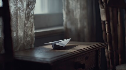 A paper airplane rests on a wooden table near a window, bathed in soft light