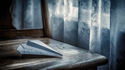 A paper airplane rests on a wooden chair, near a window with sheer curtains