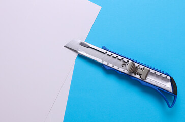 Metal stationery knife and white sheets of paper on a blue background