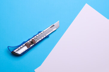 Metal stationery knife and white sheets of paper on a blue background