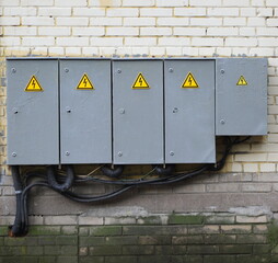 Closed metal electrical panels with high-voltage markings are hanging on a brick wall