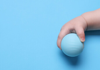 Baby's hand holding a ball for motor skills development on a blue background