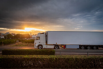 Refrigerated truck driving on a highway at sunset, under a dramatic evening sky.Side view.