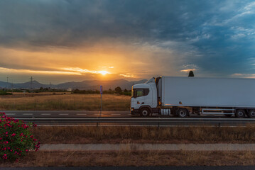 Refrigerated truck driving on a highway at sunset, under a dramatic evening sky.Side view.