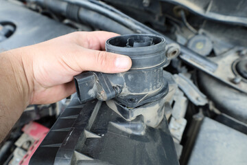 A close-up of a hand holding or installing a part in a car's engine compartment. The shot...