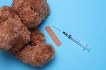 Toy bear with syringe and medical plaster on blue background. Medicine concept. Vaccinations for...