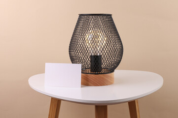 Loft lamp with white blank business card on the table, beige background
