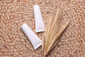 Cream tubes with dry wheat ears on a wicker mat. Natural cosmetic. Beauty concept