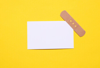 White business card with medical plaster on yellow background